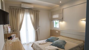 A hotel room with a bed, a TV, a window with curtains, and a bedside table with a kettle and cups. - Moonlight Hotel (Hersonissos)