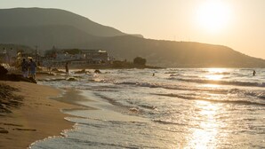 A beach with waves, a sunset, and buildings in the background. - Moonlight Hotel (Hersonissos)