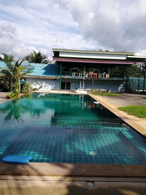 A swimming pool with a tiled deck, a covered seating area, and a building with a blue roof and a sign in a local language. - Sai Rung Resort (Krabi)