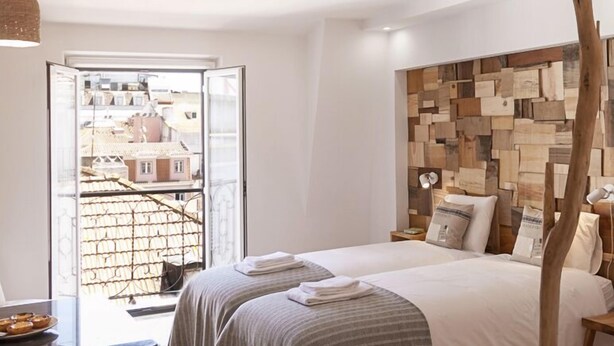 A modern bedroom with a large bed, a wooden headboard, and a view of the city through a glass door. - Bairro Studio Apartment - by LU Holidays (Lisbon)