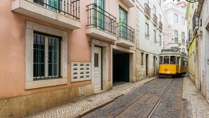 Eine enge Kopfsteinpflasterstraße, gesäumt von Gebäuden mit Balkonen, an der ein gelber Straßenbahn fährt.