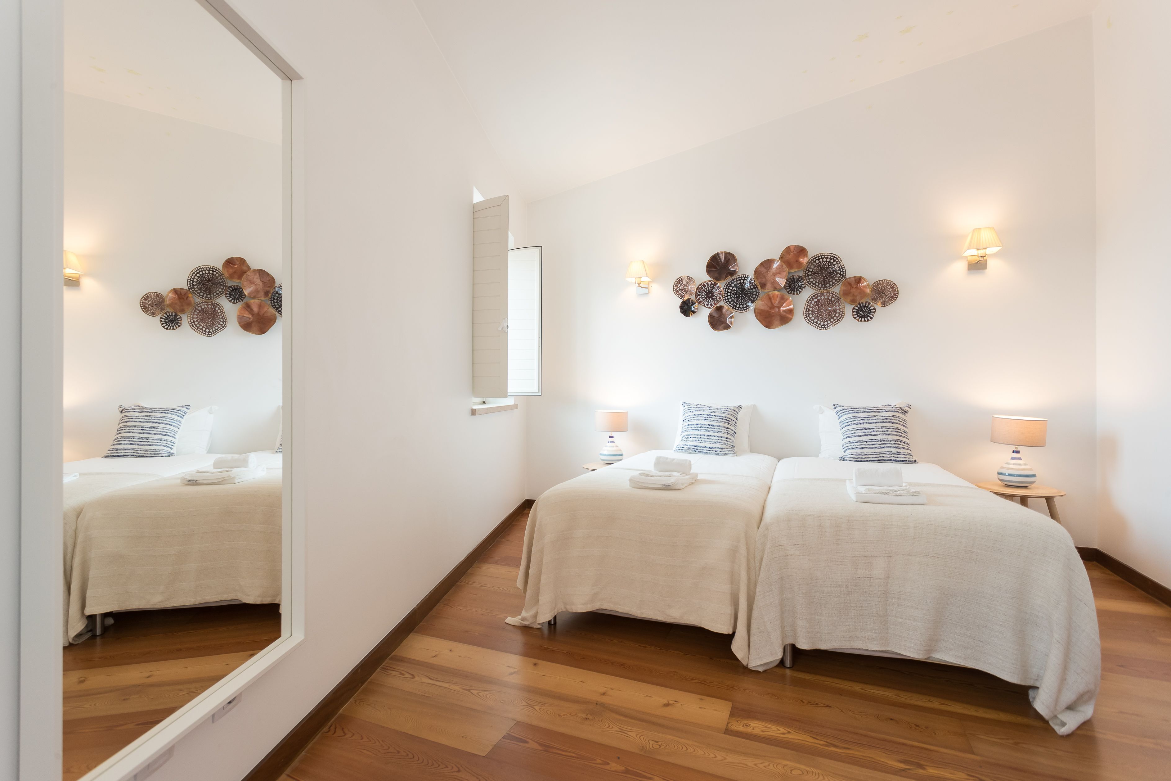 Habitación de hotel con dos camas, suelo de madera, lámparas de pared y decoración en las paredes.