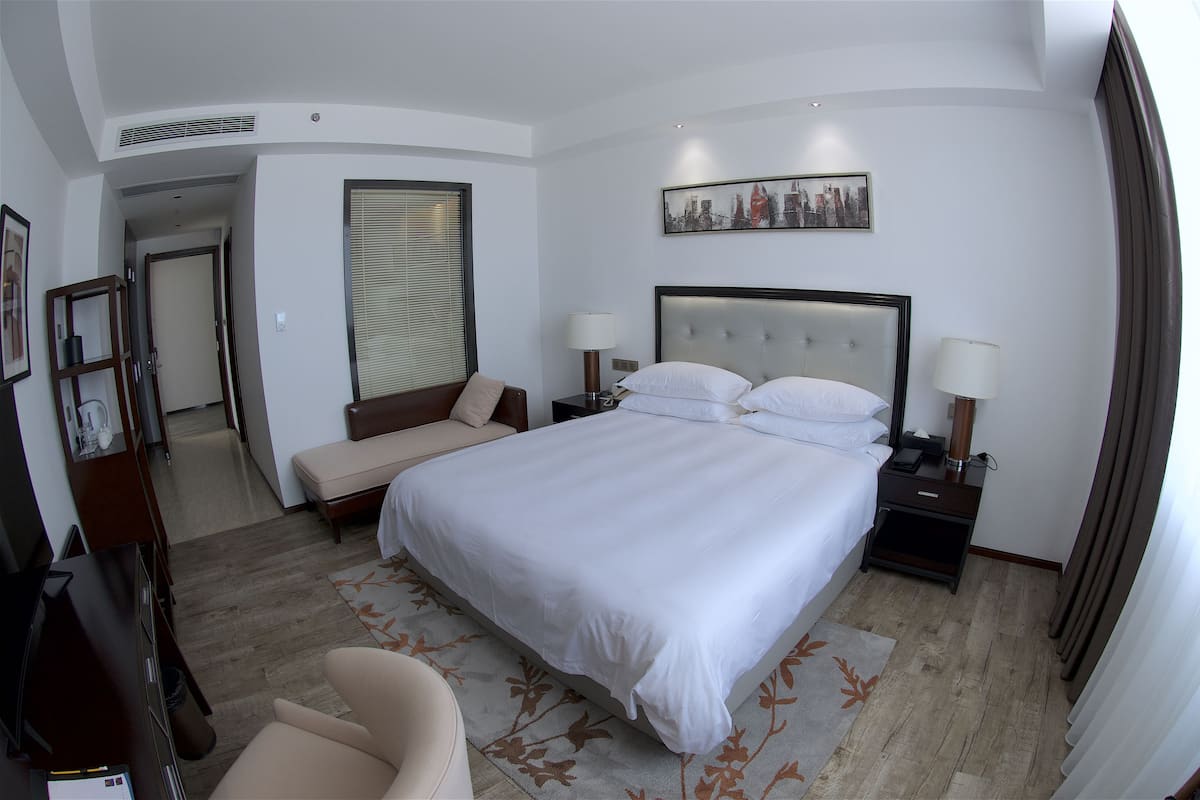 Ein Hotelzimmer mit einem großen Bett, zwei Nachttischen, einem Schlafsofa, einem Sessel und einem Bild an der Wand.