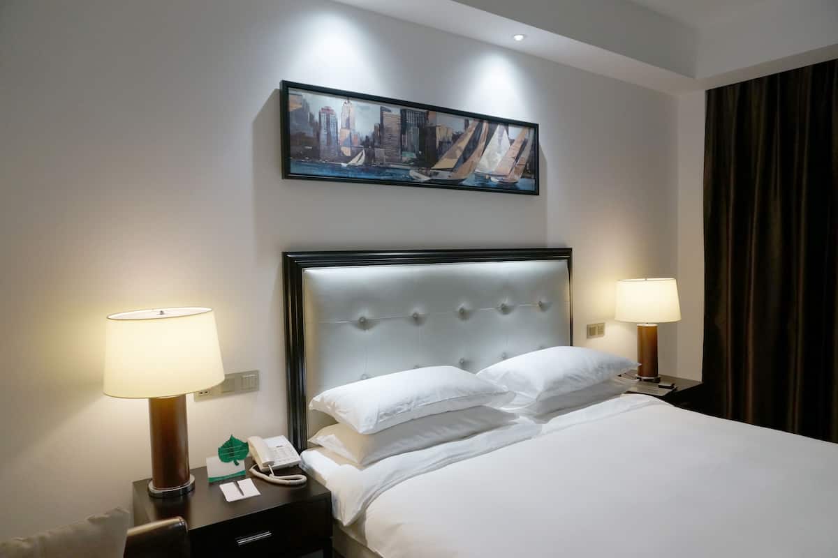 Ein Hotelzimmer mit einem großen Bett, zwei Nachttischlampen, einem Stadtbild über dem Bett und einem Telefon auf dem Nachttisch.