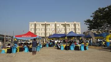 An outdoor event with tents and tables, a building in the background, and a dirt ground.