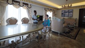 A spacious living room with a large dining table, ornate chairs, a plush sofa, and a chandelier.