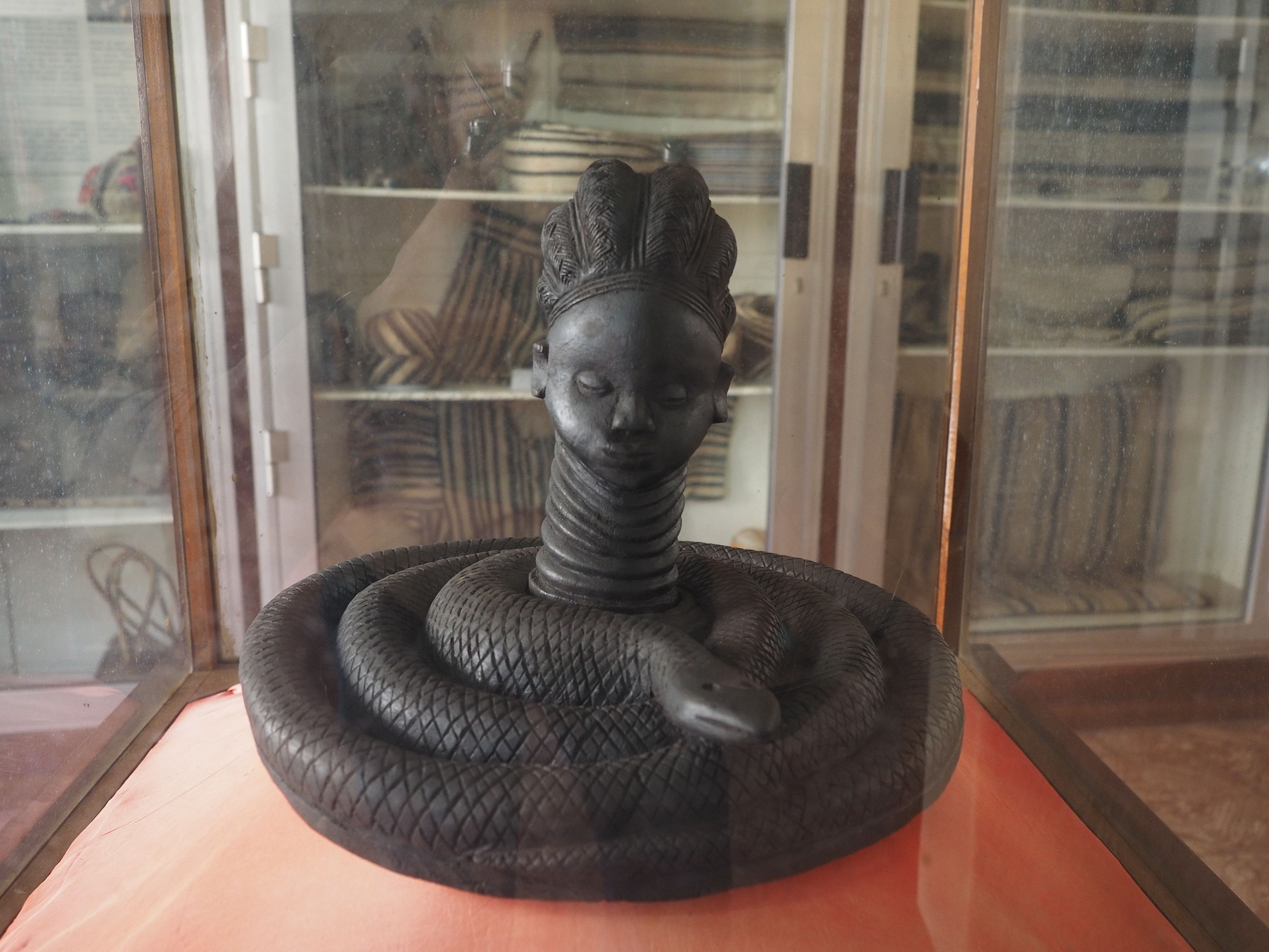 A sculpture of a figure with a snake coiled around it, displayed in a glass case.