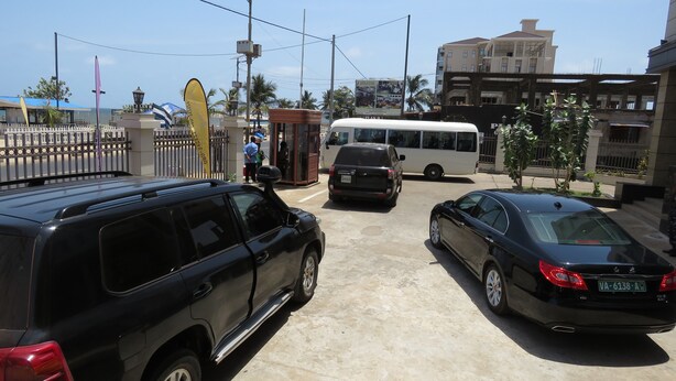 A parking area with several cars, a bus, and a gated entrance with a small kiosk. - Atlantic Lumley Hotel (Freetown)