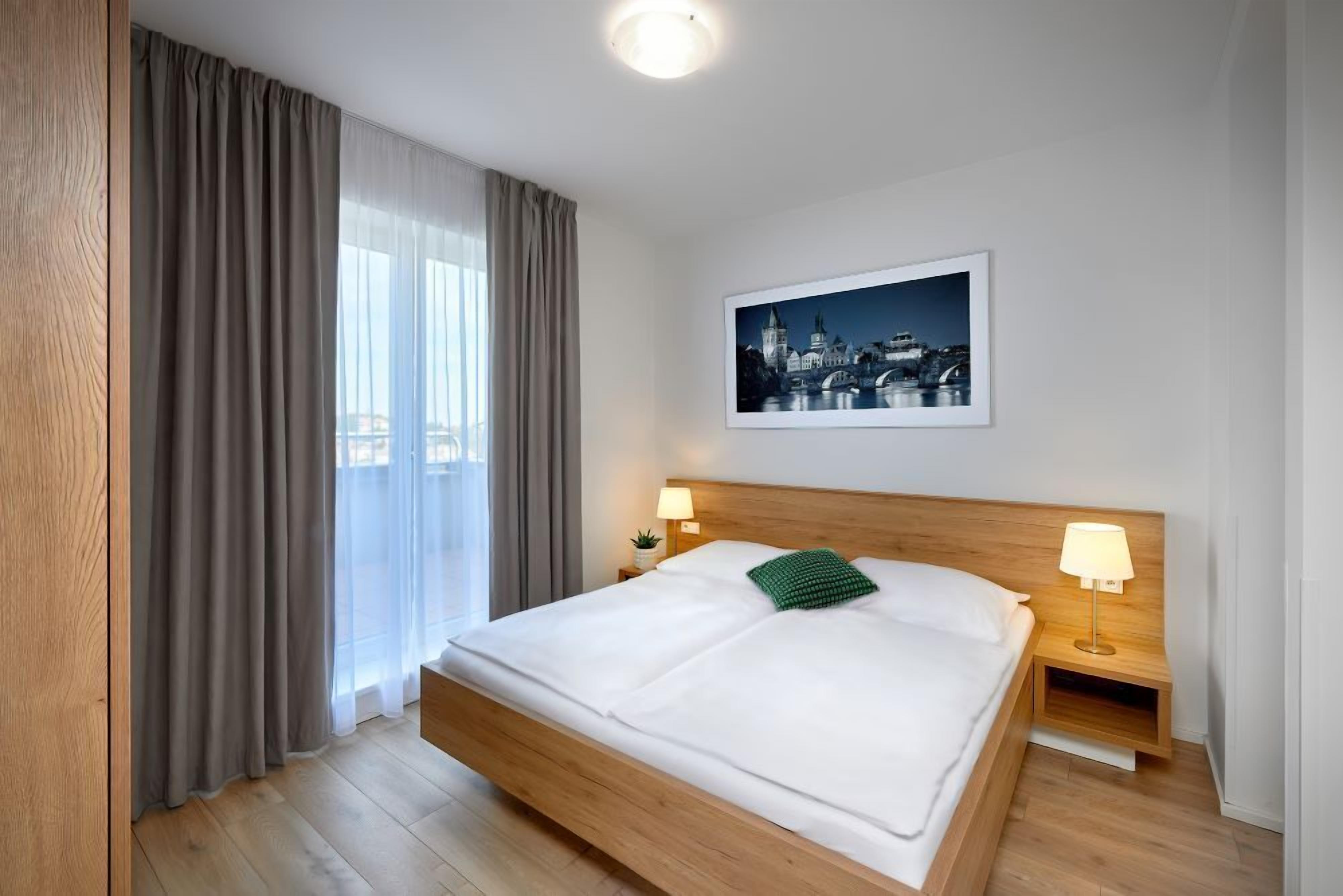 A neatly made bed with a wooden headboard, two bedside lamps, and a framed cityscape picture on the wall.