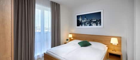A neatly made bed with a wooden headboard, two bedside lamps, and a framed cityscape picture on the wall.
