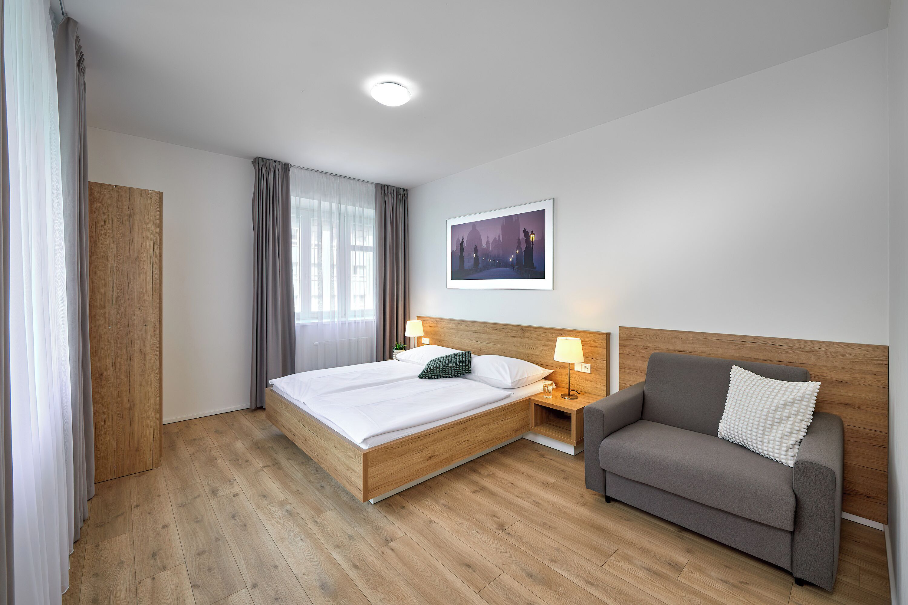 Ein Hotelzimmer mit einem Holzbett, einem grauen Sofa, einem Nachttisch mit Lampen und einem Bild an der Wand.