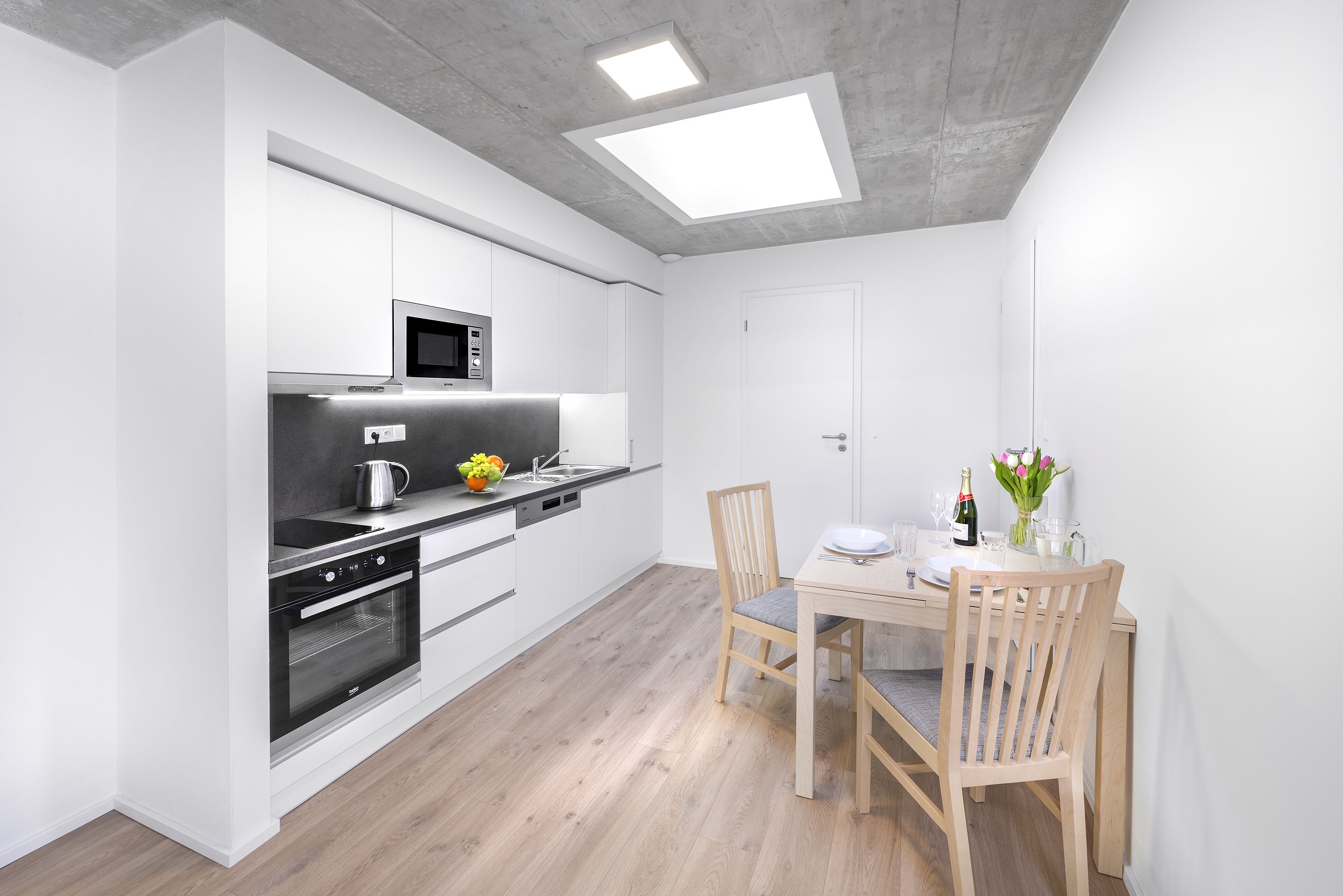 Una cocina moderna con armarios blancos, microondas, horno y una mesa de comedor con sillas.