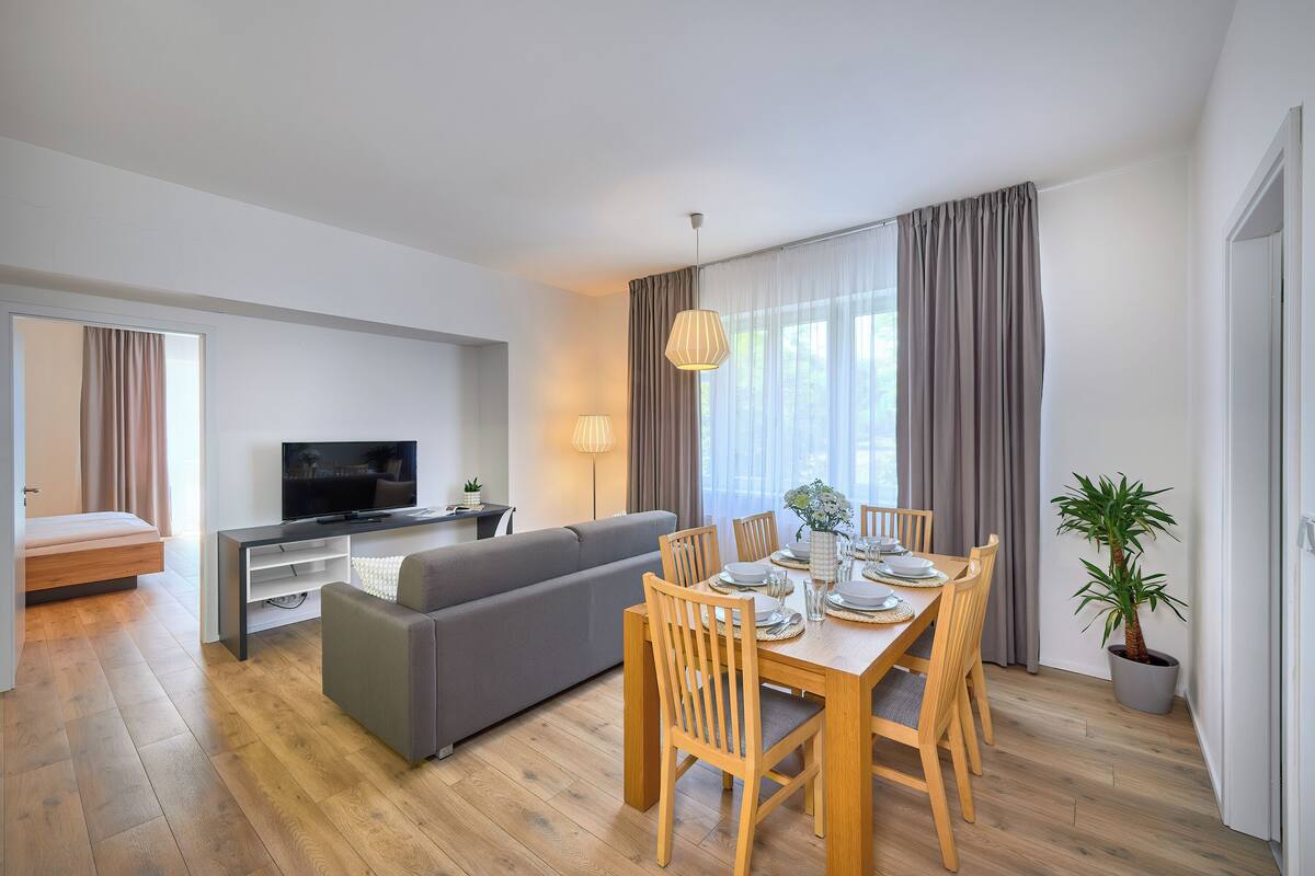 Een moderne woonkamer met een bank, eettafel, stoelen, een televisie en een potplant.