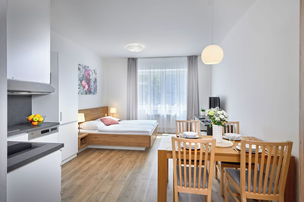 Een moderne hotelkamer met een bed, nachtkastje, lamp en een zithoek met tafel en stoelen.