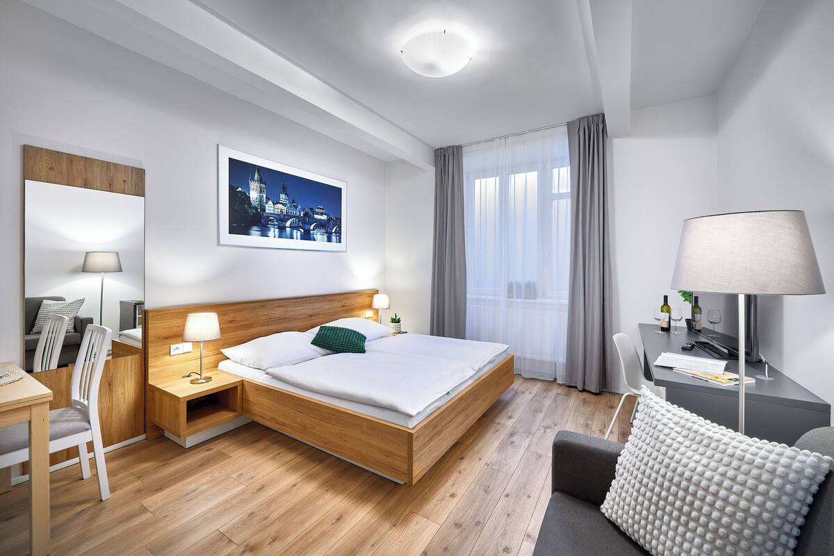 Een moderne hotelkamer met een houten bed, een bureau met een lamp, een stoel en een uitzicht op een stadsgezicht door het raam.