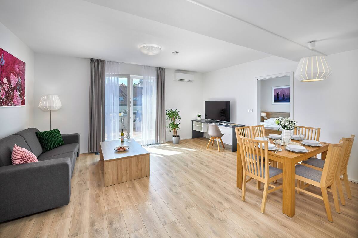 Een moderne woonkamer met een grijze bank, een houten salontafel en een eethoek met een houten tafel en stoelen.