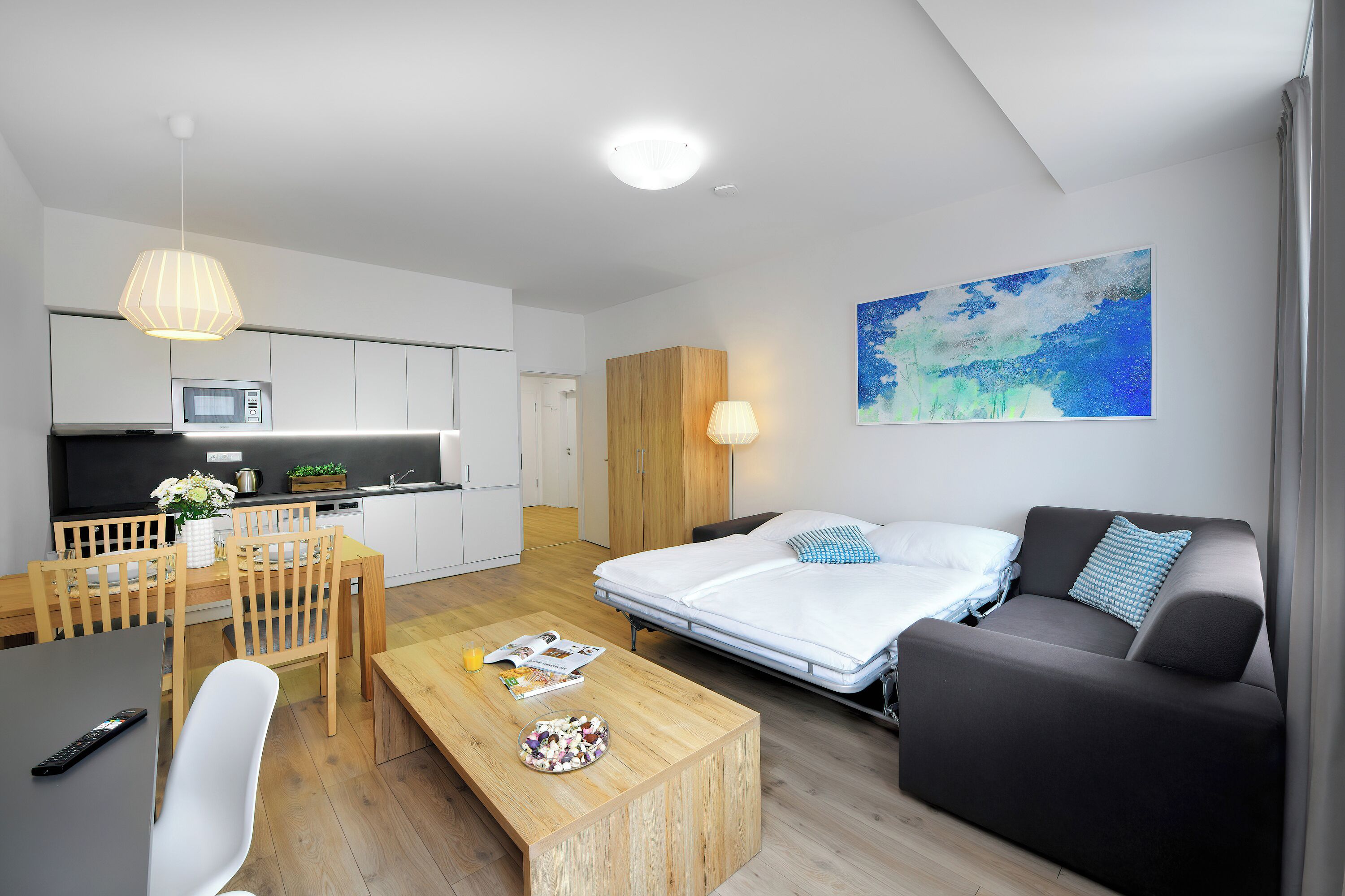 Un espacio habitable moderno y funcional con kitchenette, comedor y sofá cama.
