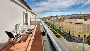A balcony with a table set for dining, overlooking a city street and buildings.
