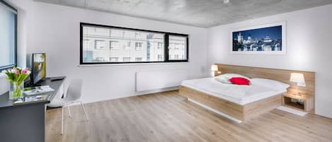 A modern bedroom with a bed, bedside table, lamp, and a large window with blinds.