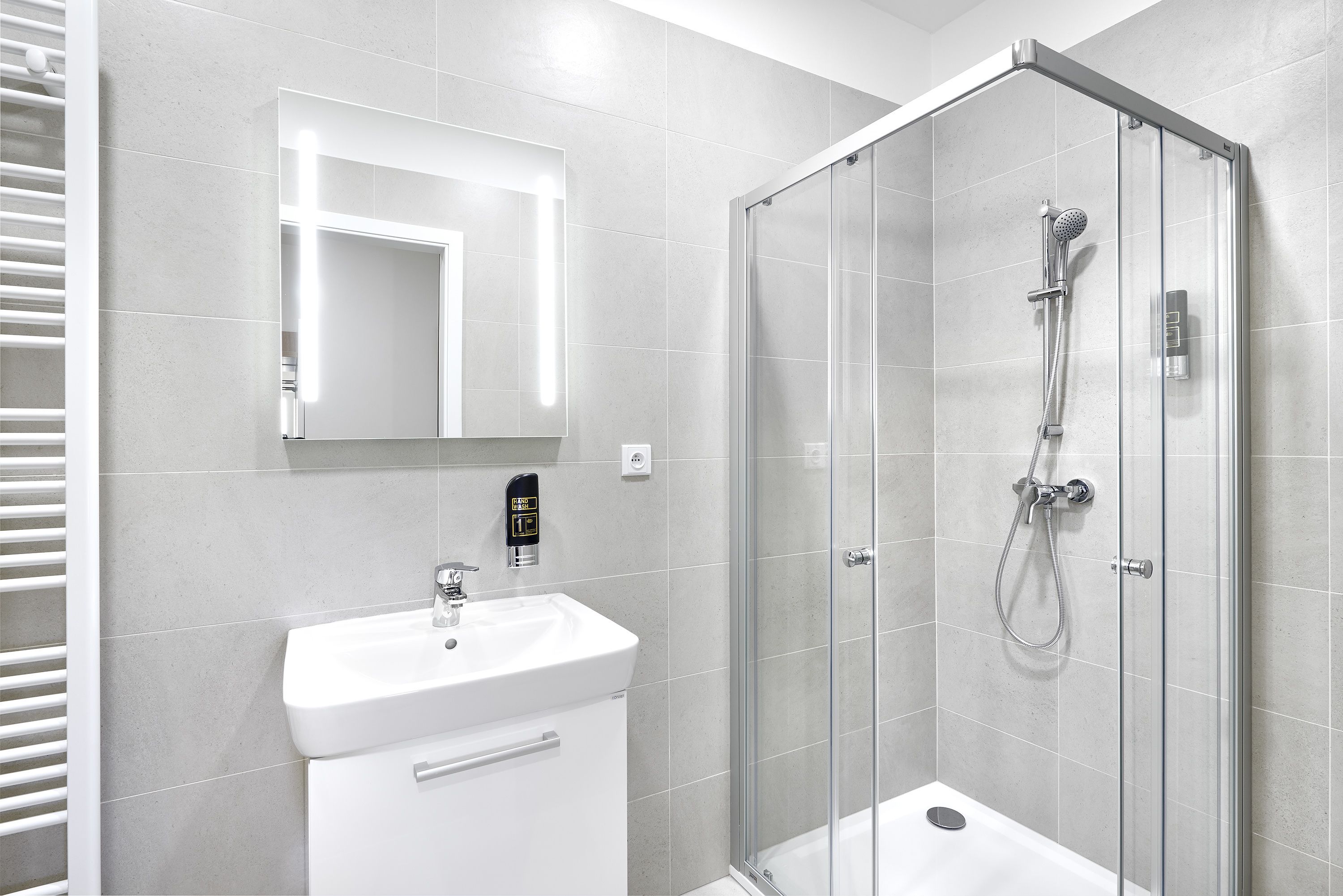 Un baño moderno con ducha envuelta en vidrio, lavamanos blanco y espejo sobre él.