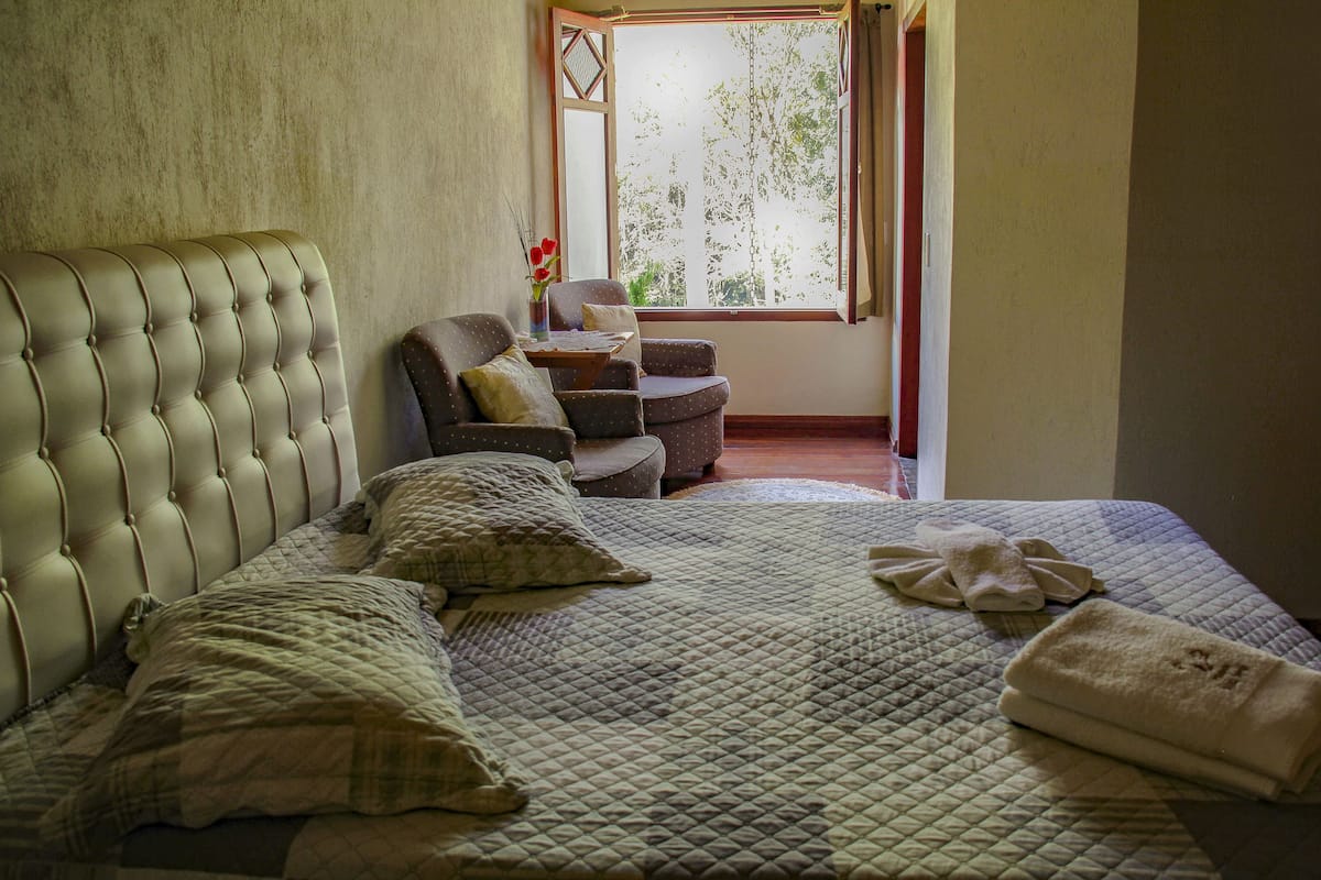 Une chambre avec un grand lit, une chaise et une fenêtre donnant sur des arbres.