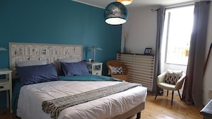 Un dormitorio con cama, mesitas de noche, cómoda, silla y ventana con cortinas.