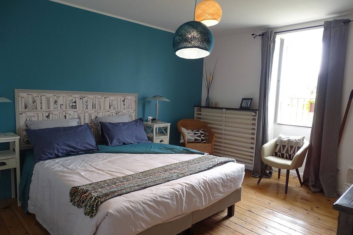 Une chambre à coucher comprenant un lit, des tables de chevet, une commode, une chaise et une fenêtre avec des rideaux.