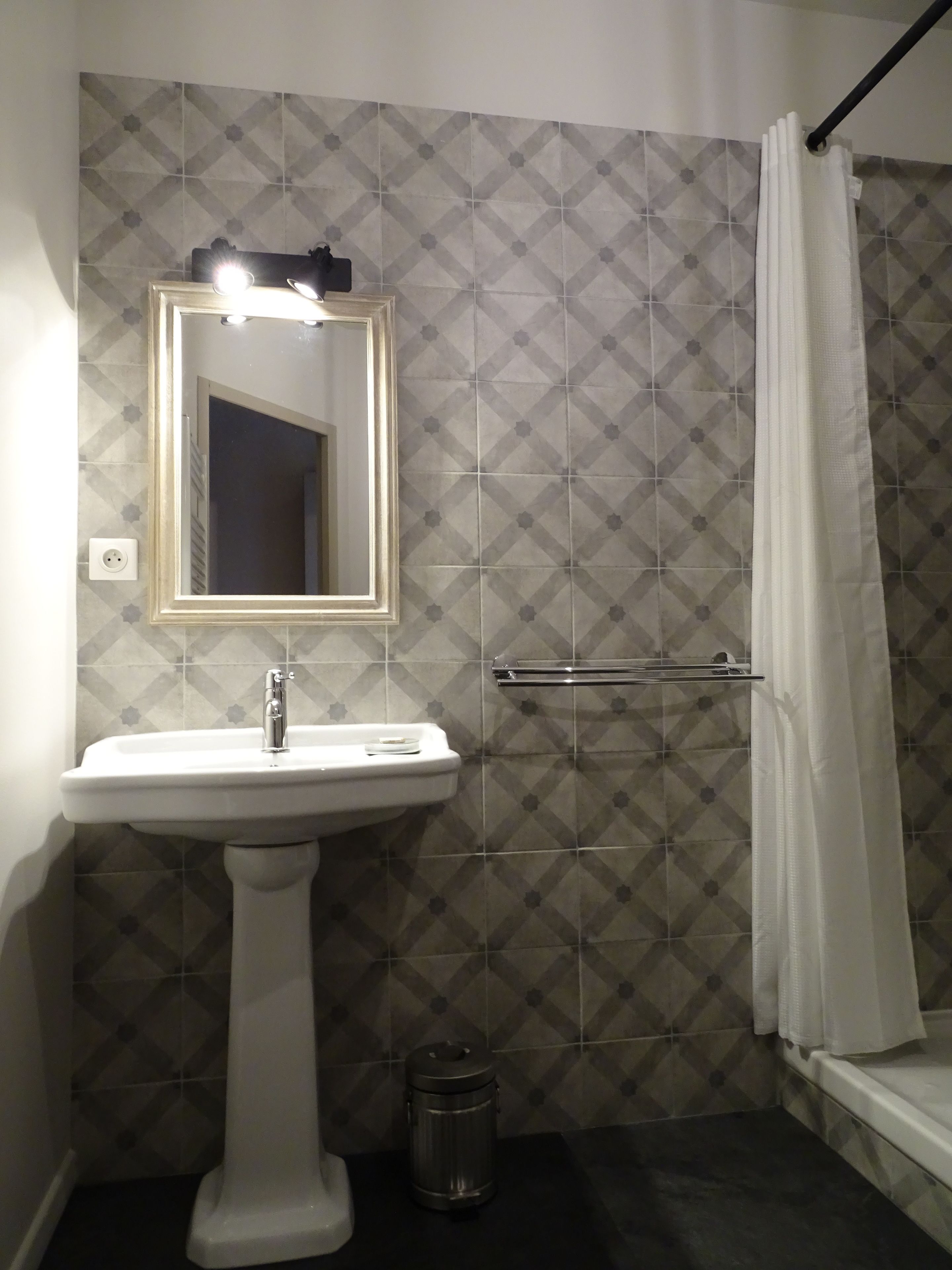 Une salle de bain avec un lavabo sur colonne, un miroir, un porte-serviettes, un rideau de douche et une poubelle.