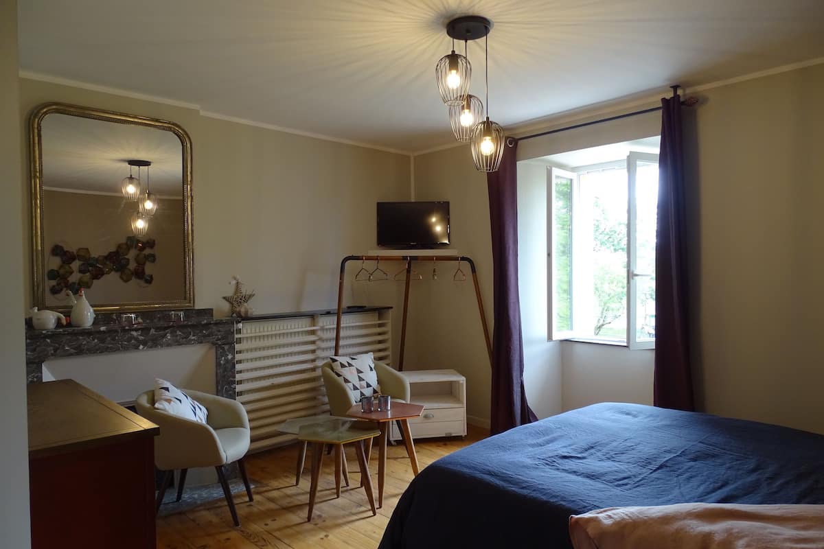 Une chambre à coucher comprenant un lit, un bureau, une chaise, une commode, un miroir, un téléviseur et une fenêtre avec des rideaux.