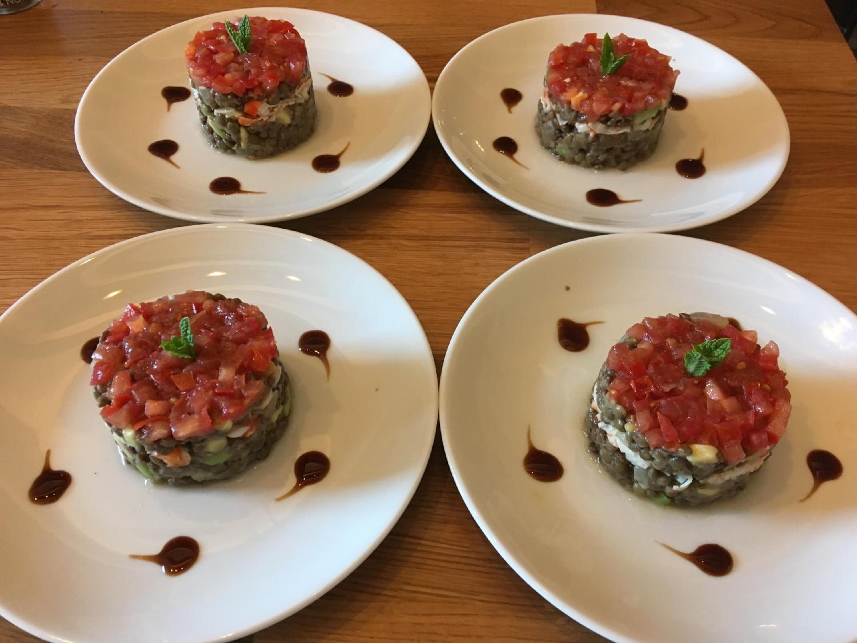 Four plates of sushi with a topping of diced red ingredients, garnished with a mint leaf, and drizzled with a dark sauce.