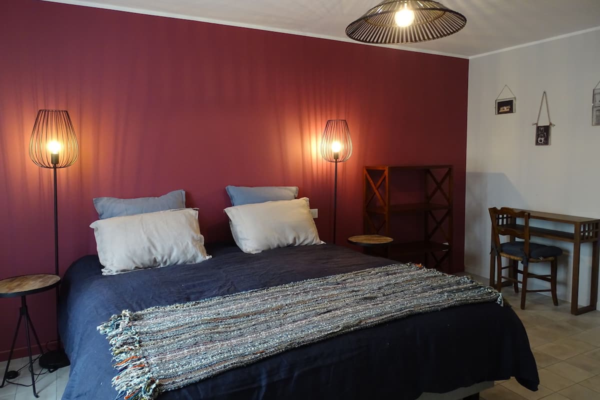 Une chambre à coucher comprenant un lit, deux lampes de chevet, une petite table ronde, une chaise en bois et un bureau avec une chaise.