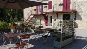 Un área de estar al aire libre con mesas y sillas, una escalera que lleva a un balcón y una jardinera con flores.
