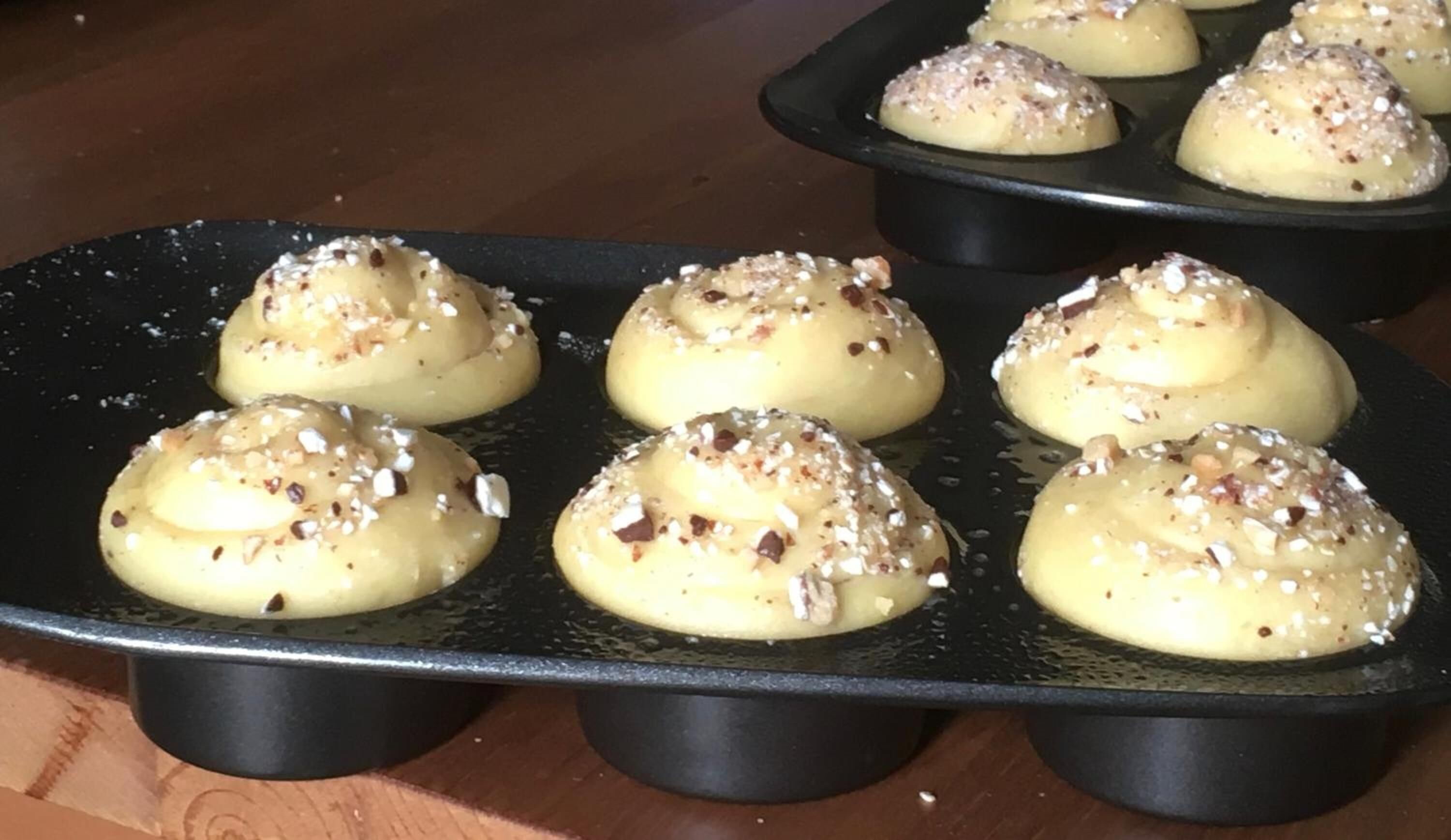 A muffin tray with six muffins topped with nuts and sugar.