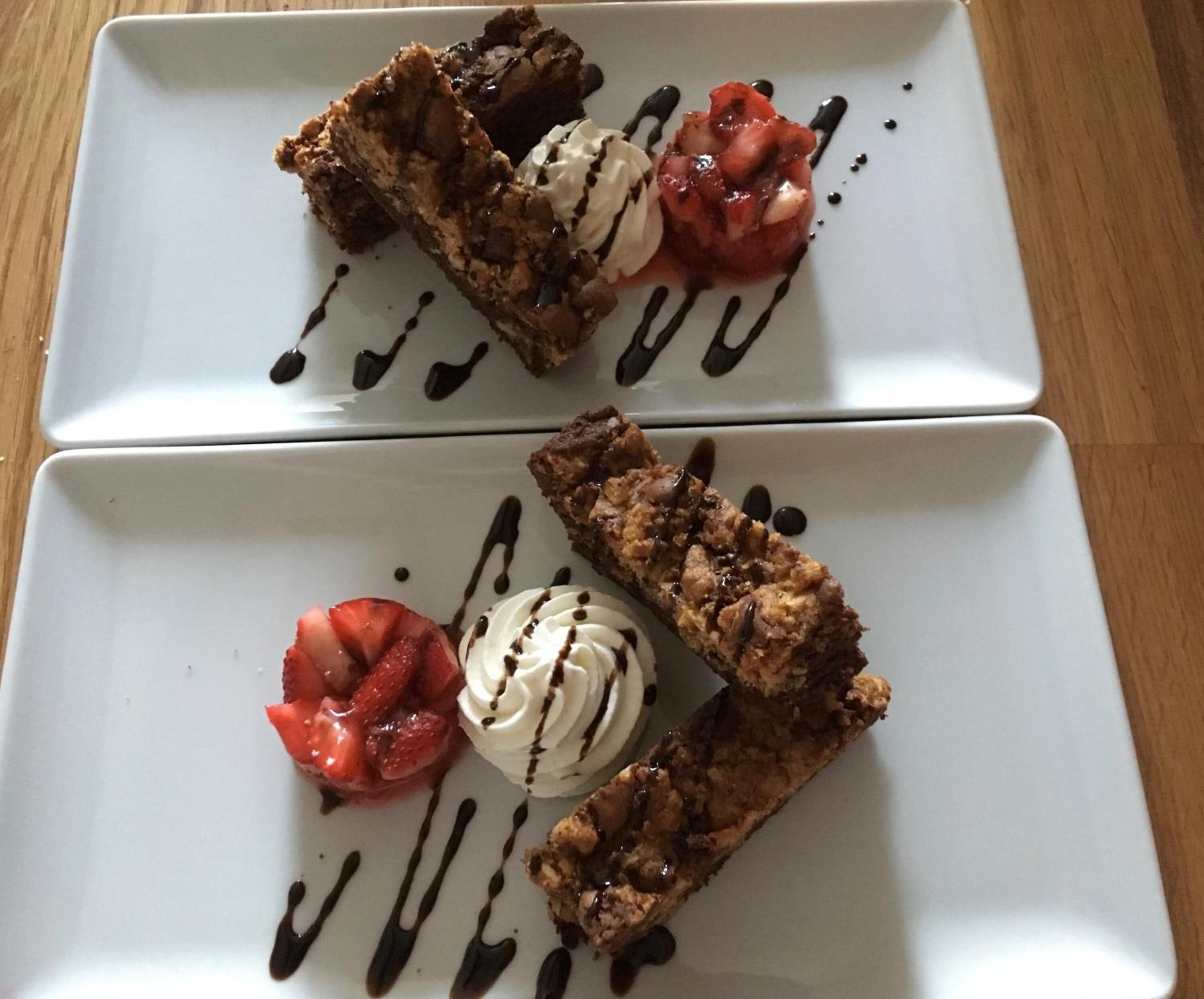 Dos platos rectangulares blancos con postres, incluyendo un brownie y una porción de helado, sobre una mesa de madera.