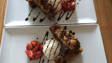 Dos platos rectangulares blancos con postres, incluyendo un brownie y una porción de helado, sobre una mesa de madera.
