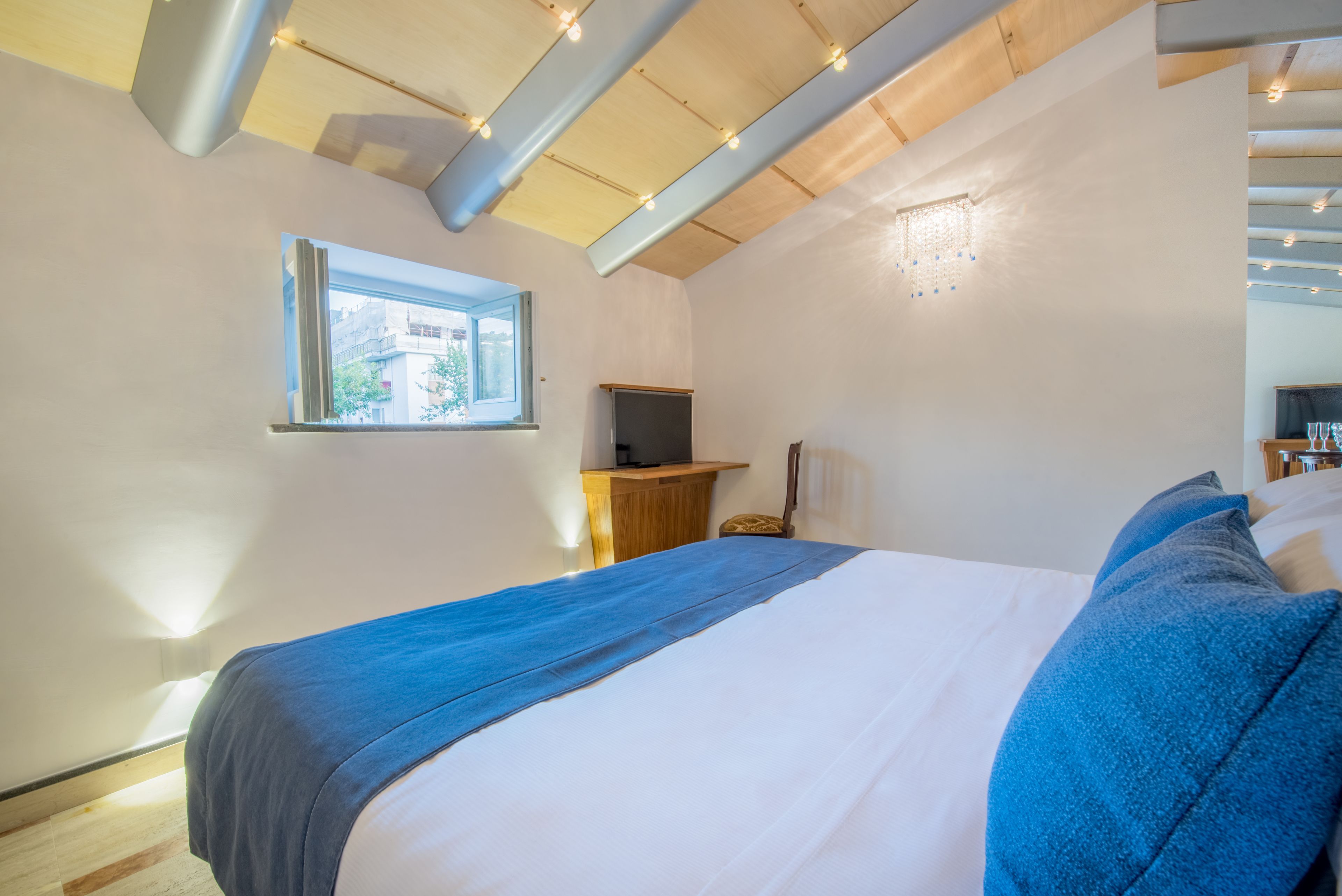 A bedroom with a bed, a television, a window, and a ceiling light fixture.