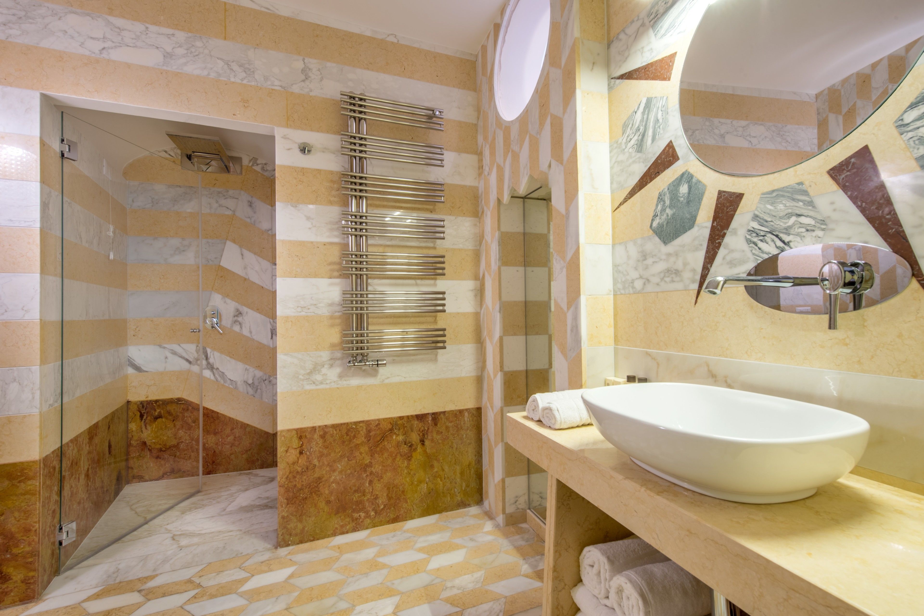 Un bagno moderno con cabina doccia in vetro, parete rivestita in marmo, lavandino bianco e porta asciugamani.