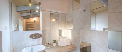 A modern bathroom with a large marble sink, a wooden vanity, and multiple mirrors.