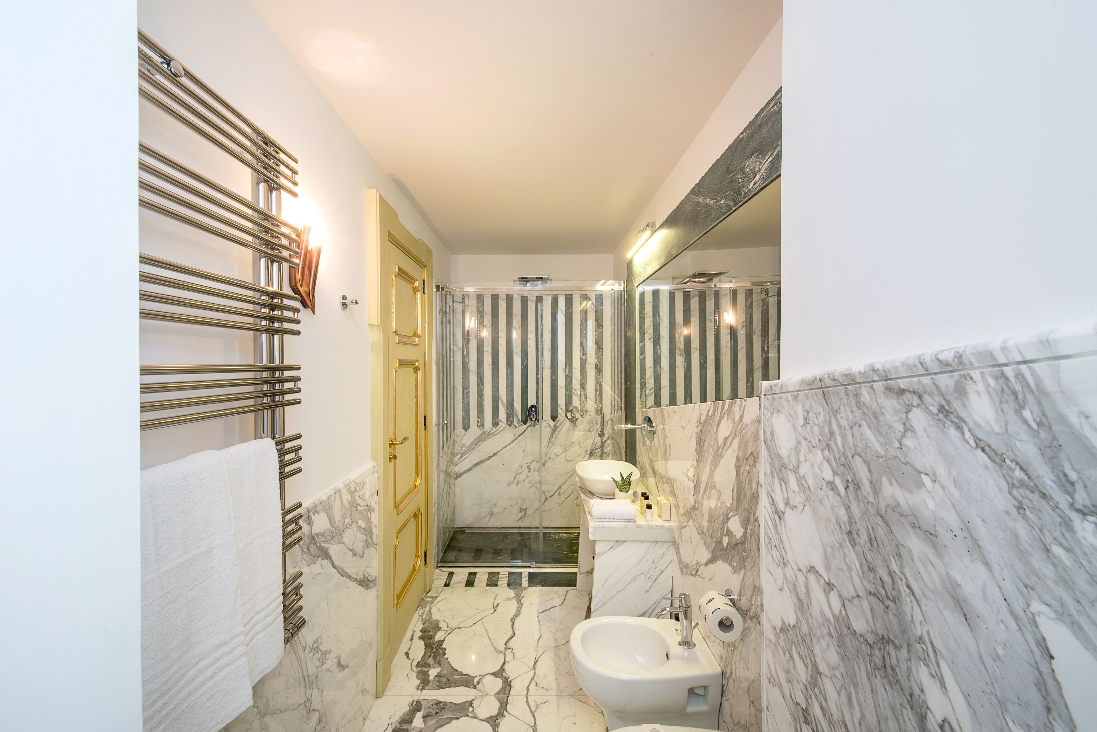 A modern bathroom with a marble floor, a glass shower enclosure, and a gold-framed door.