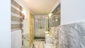 A modern bathroom with a marble floor, a glass shower enclosure, and a gold-framed door.