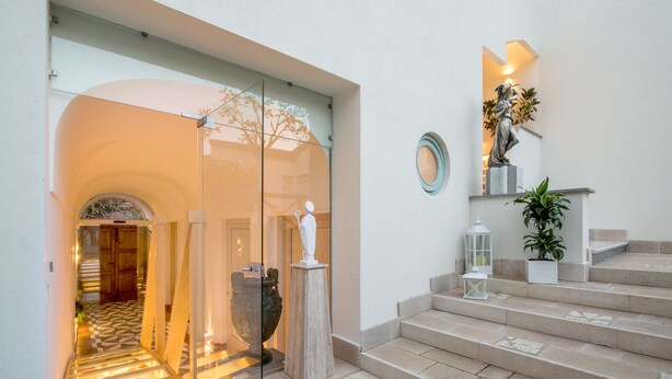 Una entrada de hotel moderna con puerta de cristal, una estatua, una escalera y una planta en maceta.
