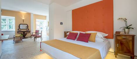 A spacious bedroom with a large bed, a wooden nightstand, and a bright orange accent wall.