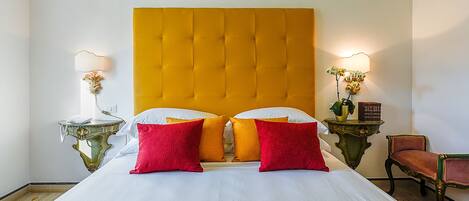 A hotel room with a large bed, two bedside tables with lamps, a chair, and a small table with a plant.