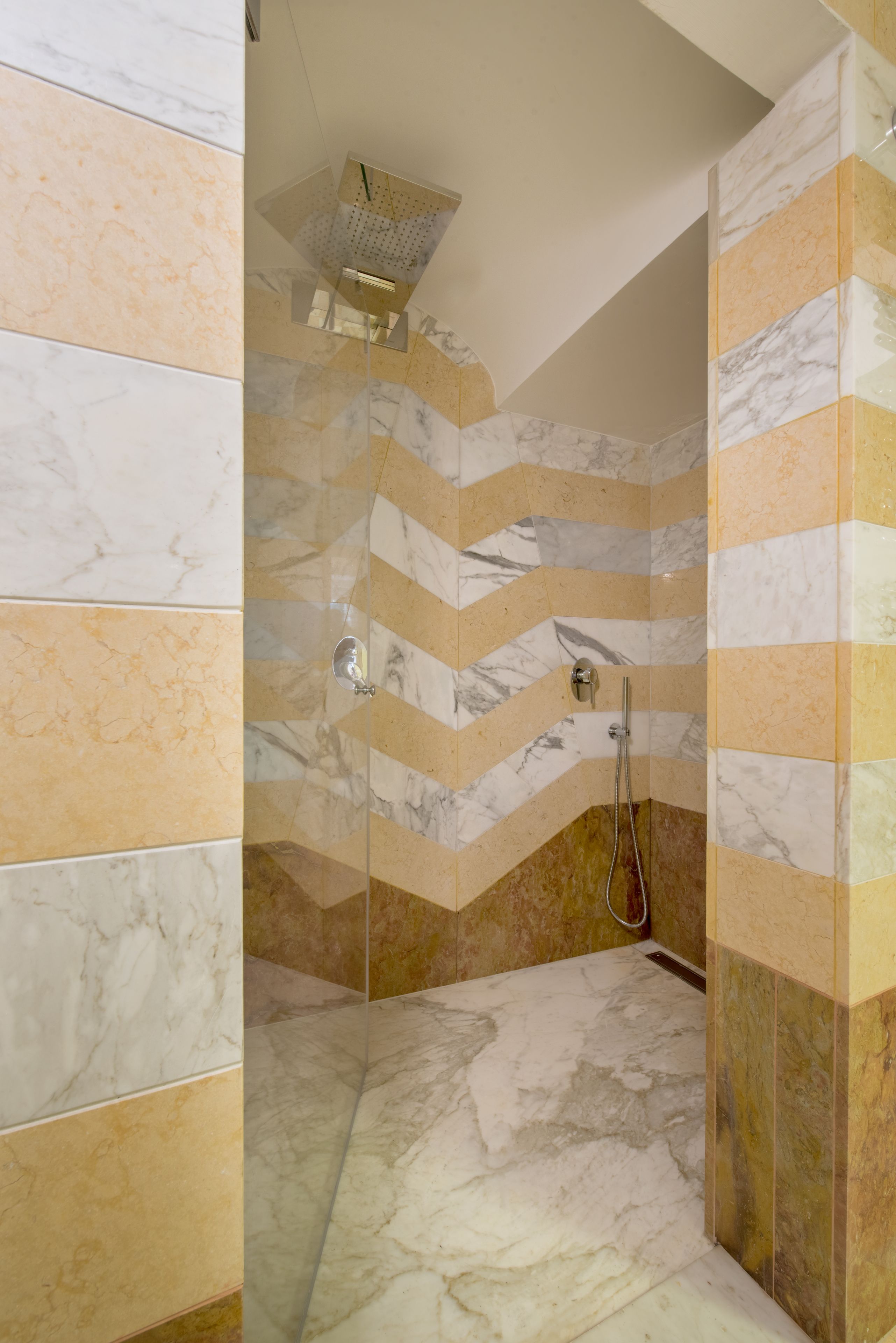 A shower with a glass door, marble walls, and a chevron pattern.