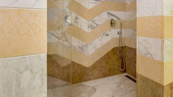 A shower with a glass door, marble walls, and a chevron pattern.