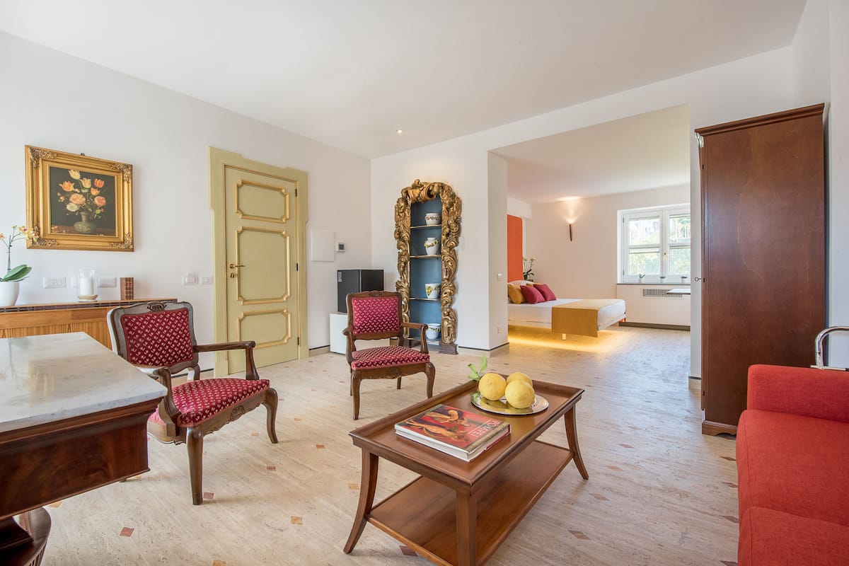Amplia sala de estar con una mesa de centro de madera, dos sillones tapizados de rojo, una estantería y un ventanal grande.