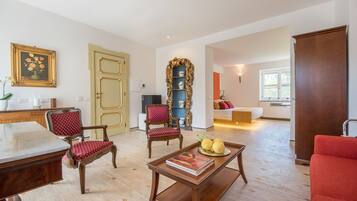 A spacious living room with a wooden coffee table, two red upholstered chairs, a bookshelf, and a large window.