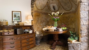 Una habitación con un aparador de madera, una mesa con comida y flores, y una pared de piedra con un mural.