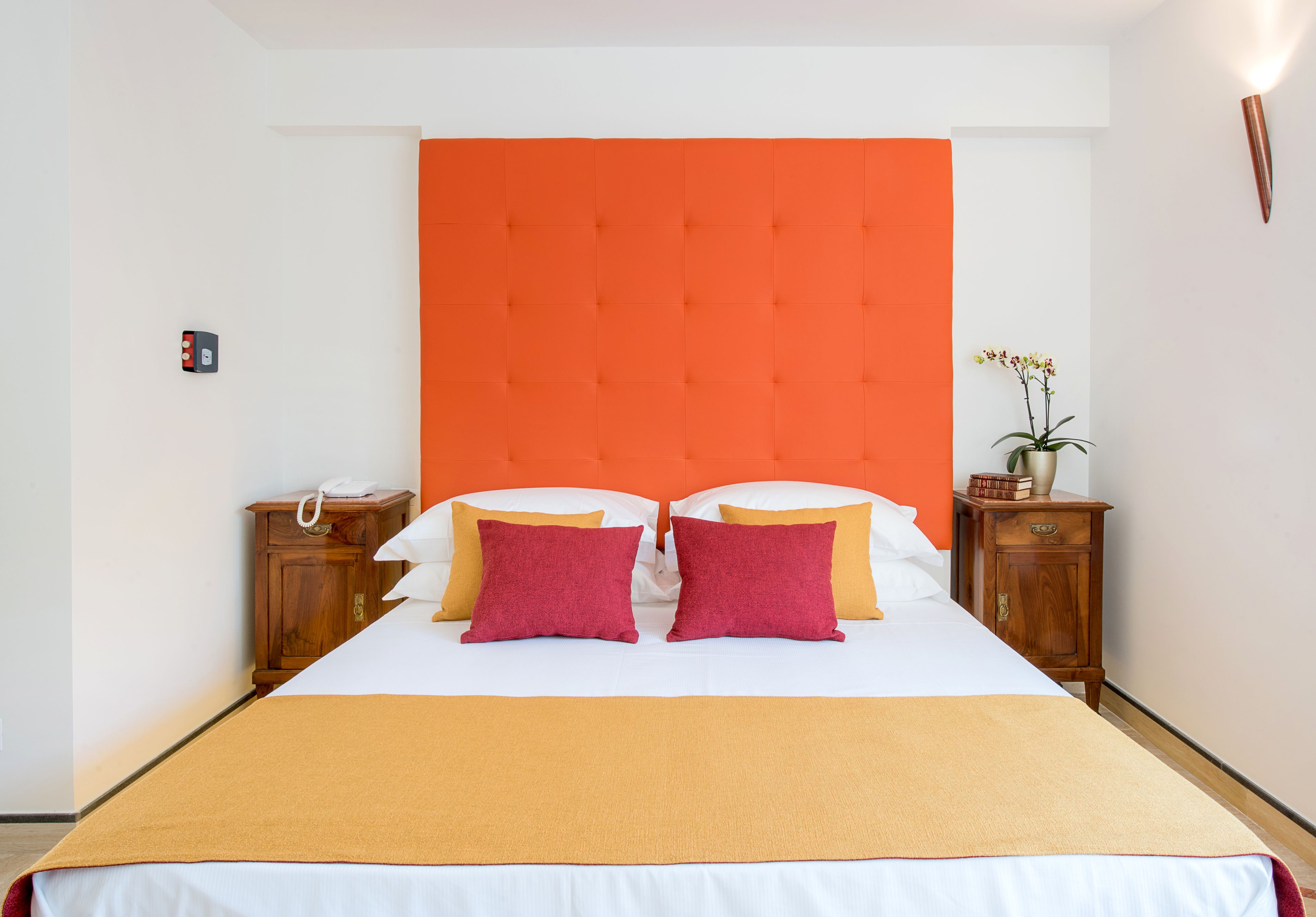 Een hotelkamer met een groot bed, een oranje hoofdeinde, houten nachtkastjes en een kleine potplant.