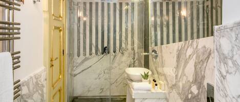 A modern bathroom with marble flooring, a large mirror, two sinks, and a shower area.